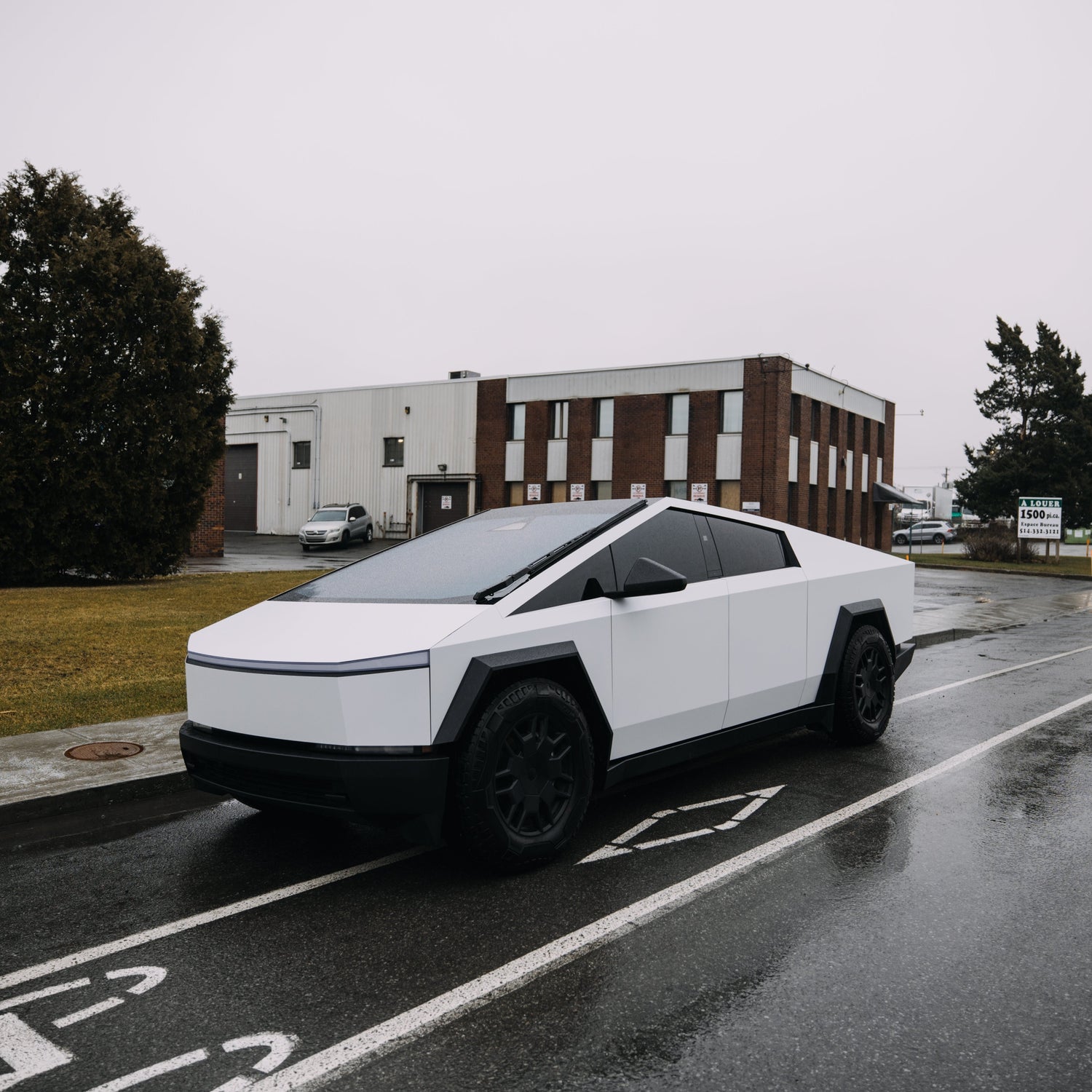A white wrapped Cybertruck parked outside on a rainy day